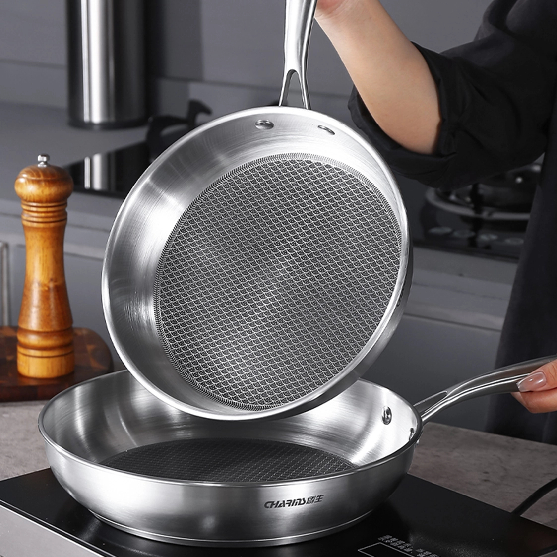 A woman cooks on a stove, using two frying pans to prepare a meal.