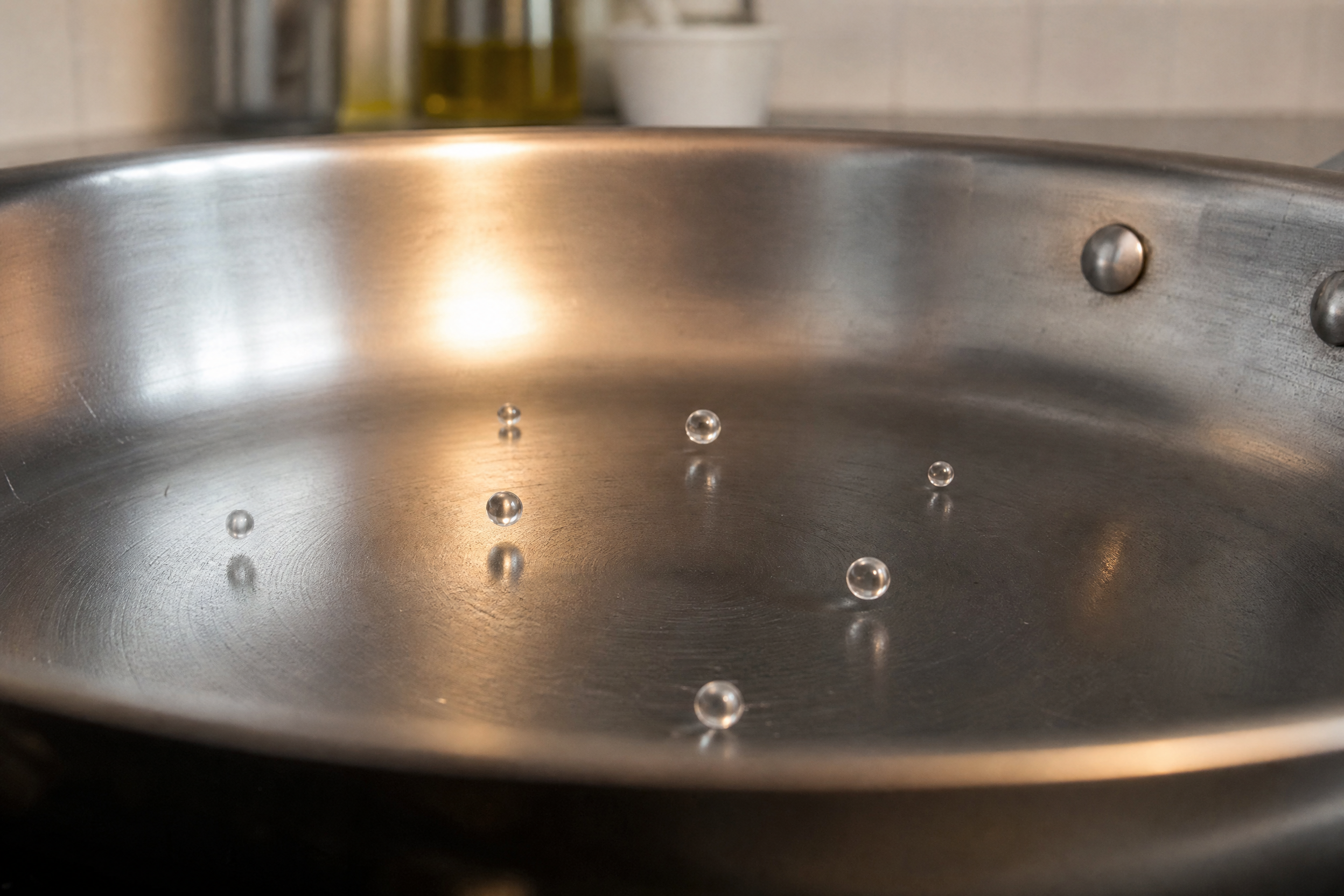 Water droplets beading and rolling on a preheated stainless steel pan surface demonstrating the Leidenfrost effect