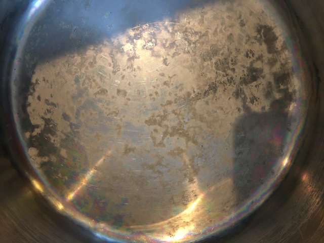 Close-up photograph of corrosion pitting on a stainless steel pan surface showing small holes and surface damage