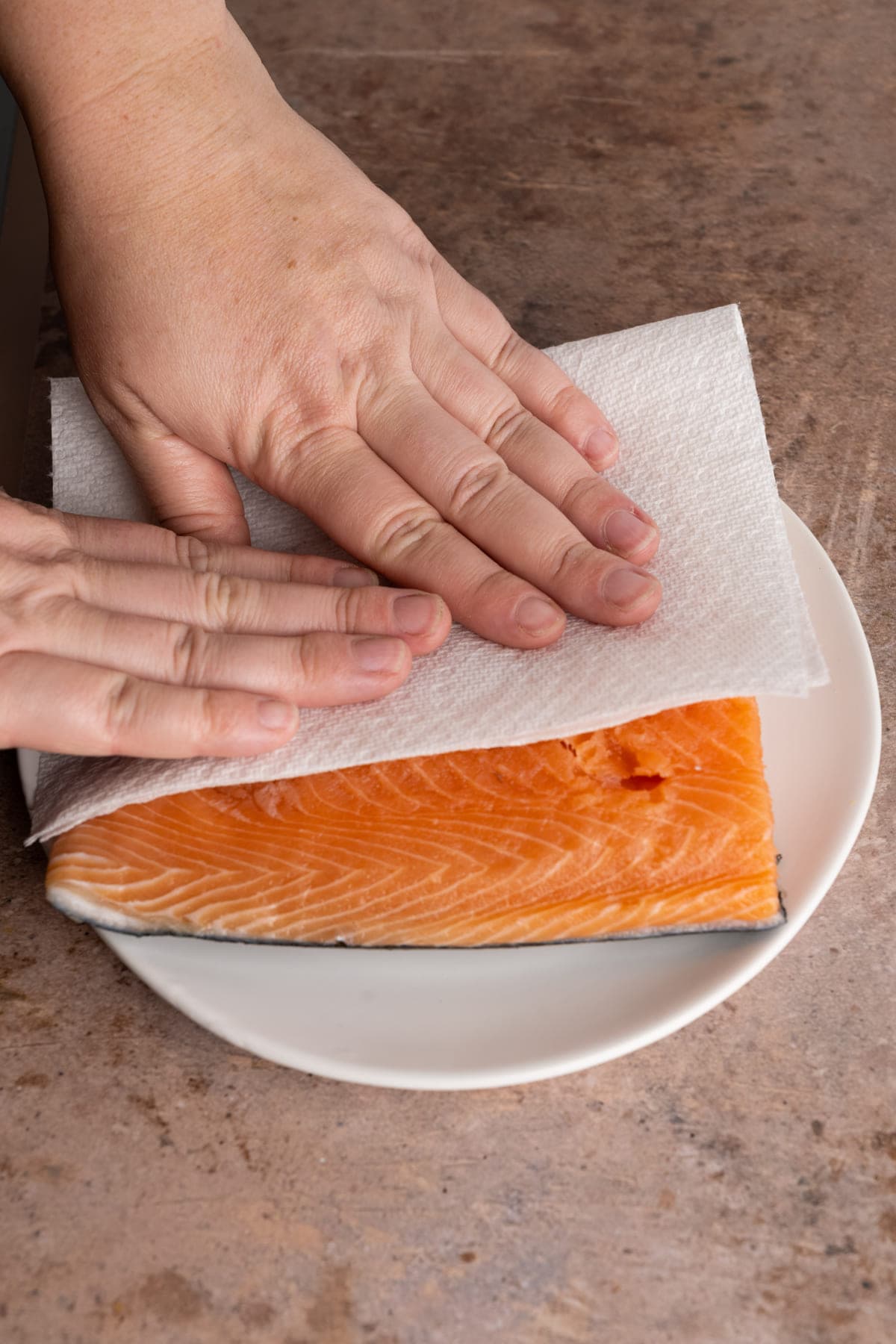 salmon fillet being patted dry with paper towels before cooking in stainless steel pan - removing surface moisture for better sear