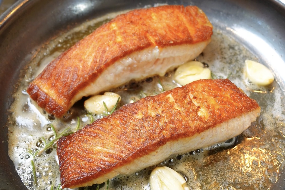 skin-on salmon fillet cooking skin-side down in stainless steel skillet showing golden crispy skin forming - proper technique