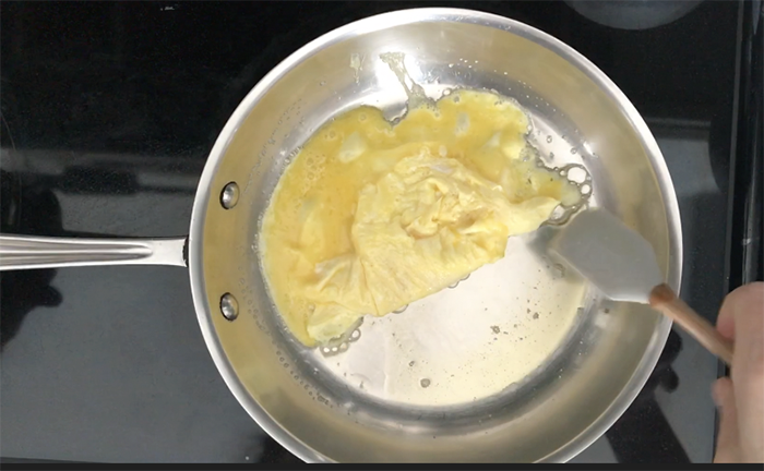 Creamy scrambled eggs cooking in stainless steel pan with silicone spatula showing glossy undercooked stage when eggs should be removed from heat