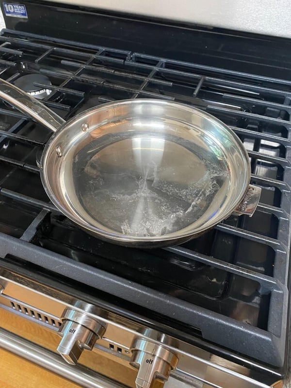 Wiping a thin layer of avocado oil onto stainless steel pan for seasoning - paper towel spreading oil on pan surface