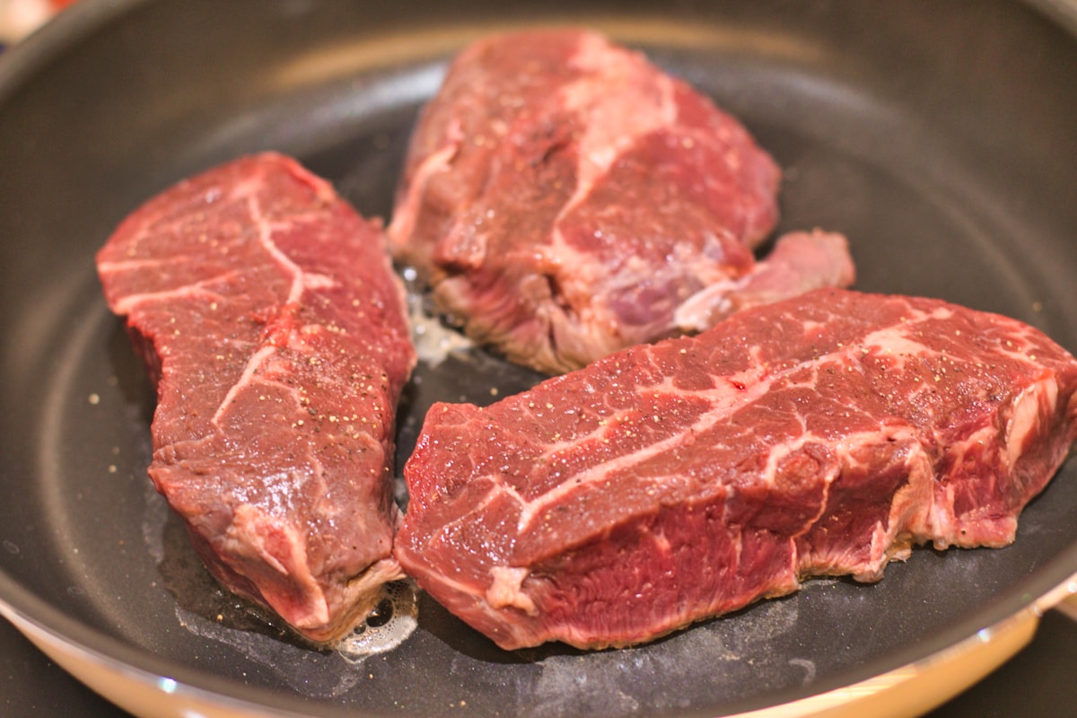 Steak forming sear crust in stainless steel pan natural release technique - golden brown crust visible on meat surface