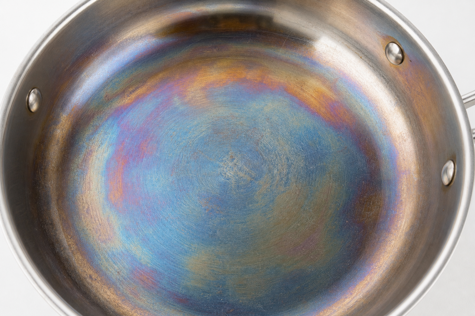 Rainbow iridescent heat tint on stainless steel pan surface — blue gold discoloration caused by chromium oxide layer thickening