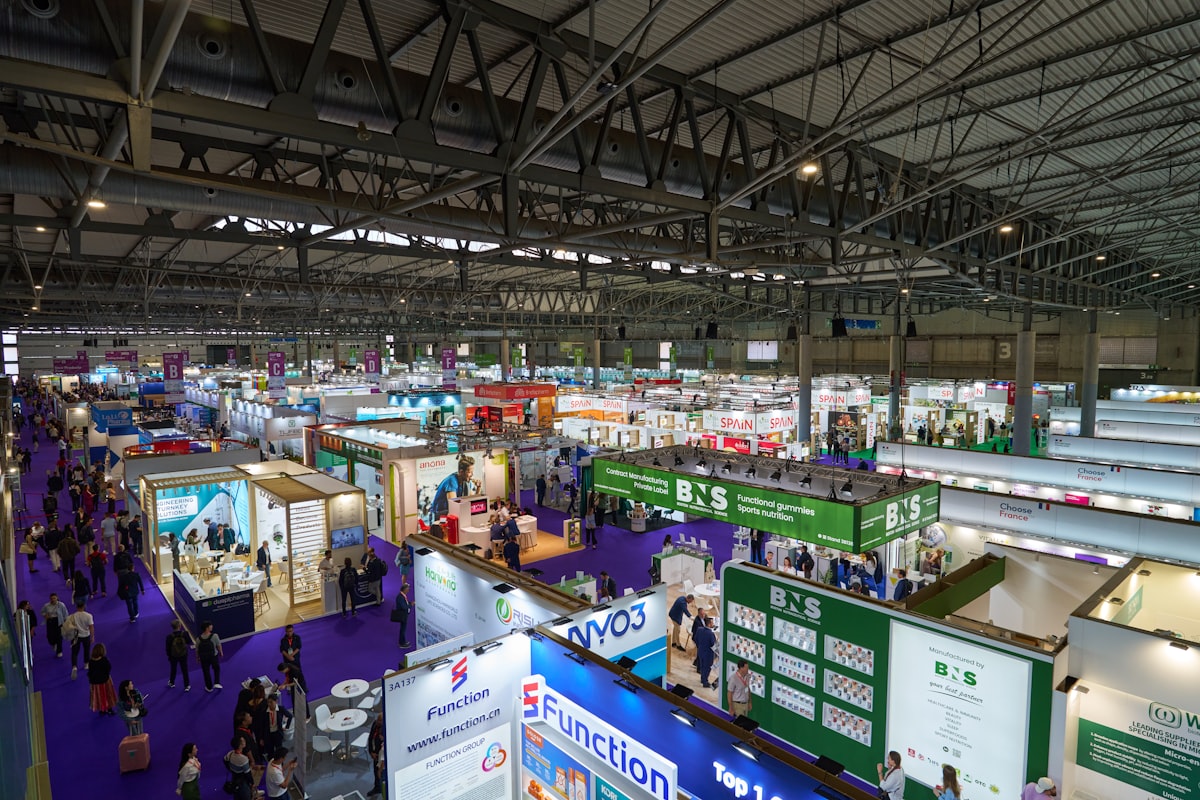 Indoor trade show exhibition hall with cookware and kitchenware vendors showing B2B buyers examining products at booths