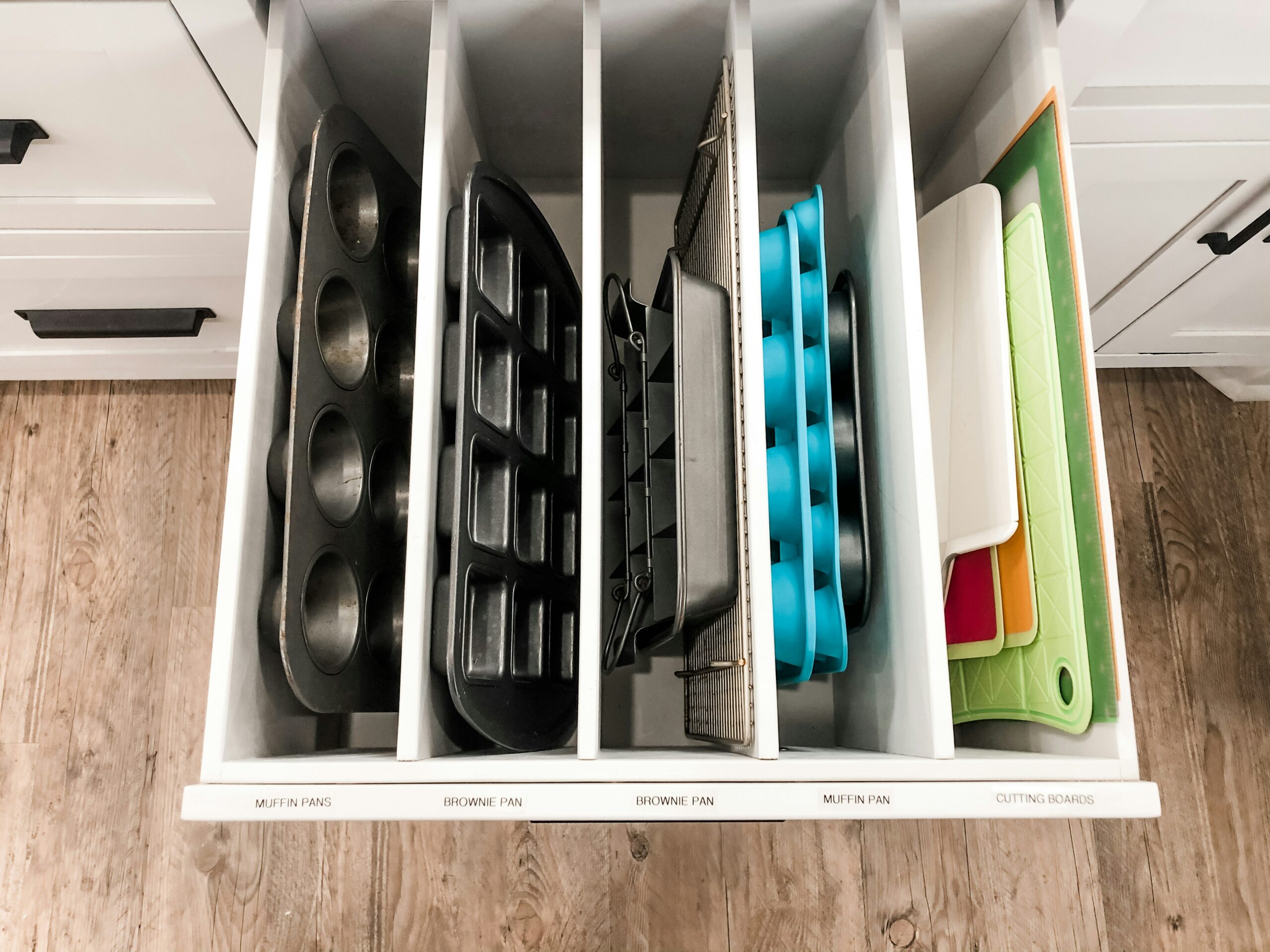 Vertical pan organizer inside a kitchen cabinet drawer with pans standing on edge in separate slots - no contact between pans