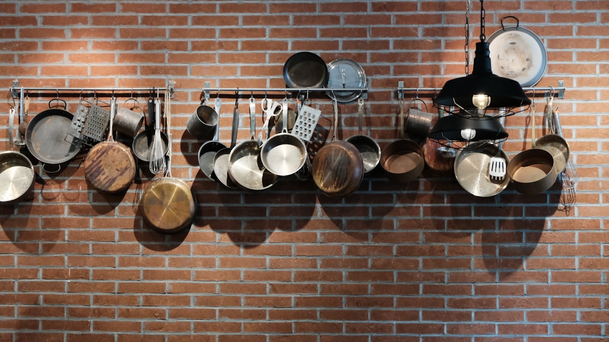 Assorted pots and pans hanging on a wall-mounted rack in a kitchen - ideal scratch-free stainless steel storage method