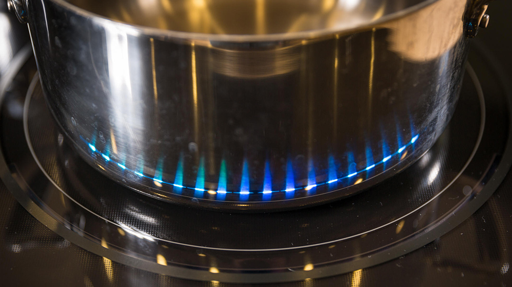 Refrigerator magnet held against the base of a stainless steel cookware pan showing induction compatibility test method