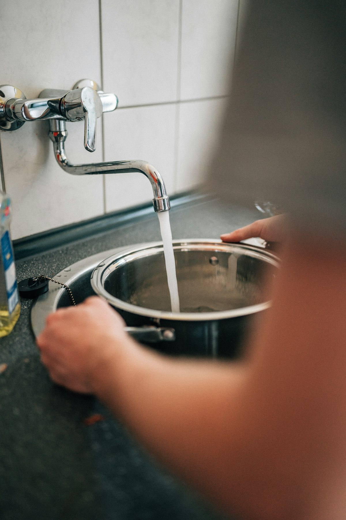 Person washing stainless steel pan with dish soap and soft sponge — proper daily cleaning technique